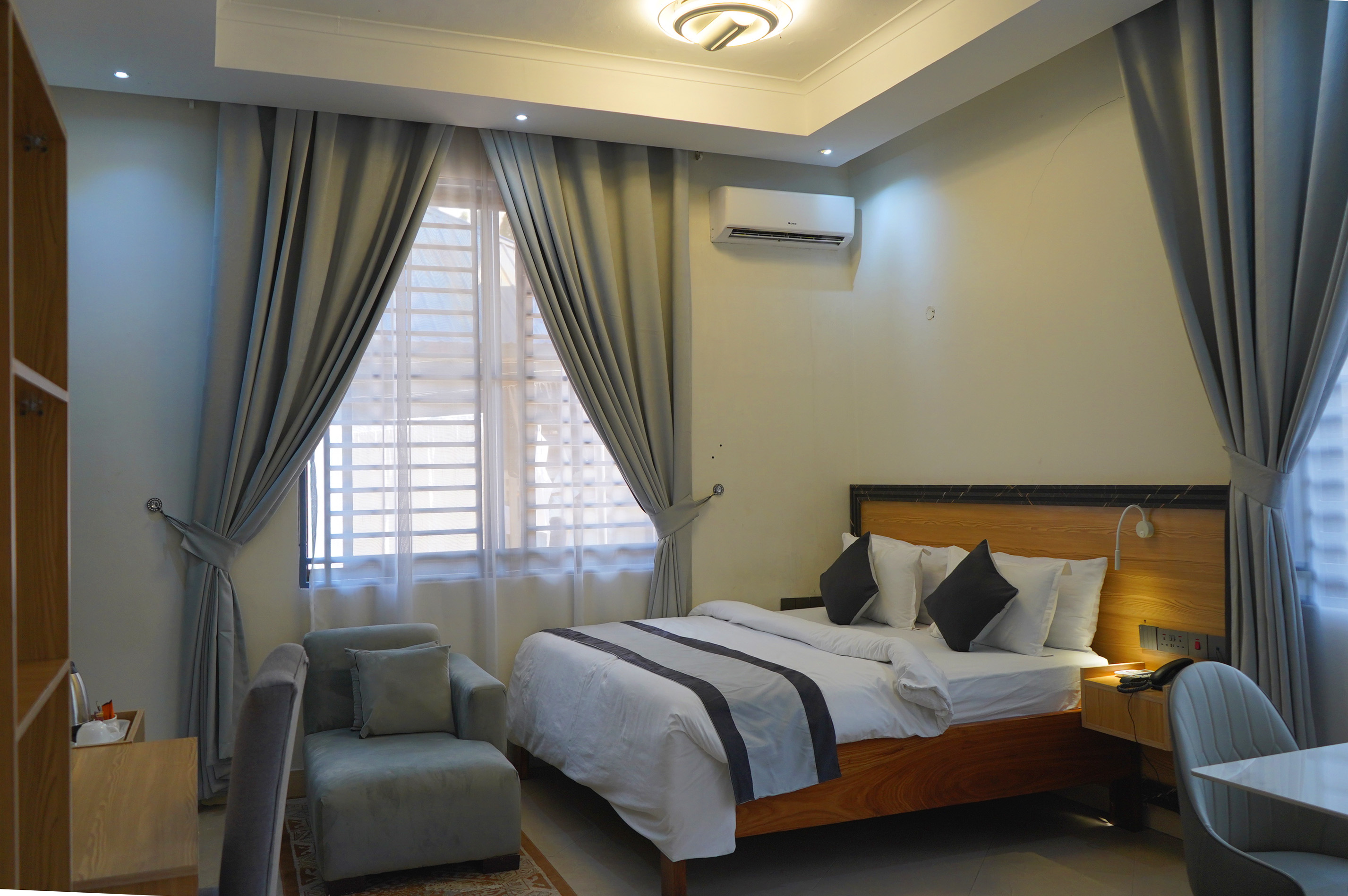 Angled room view with bed, armchair, table and floor-to-ceiling curtains
